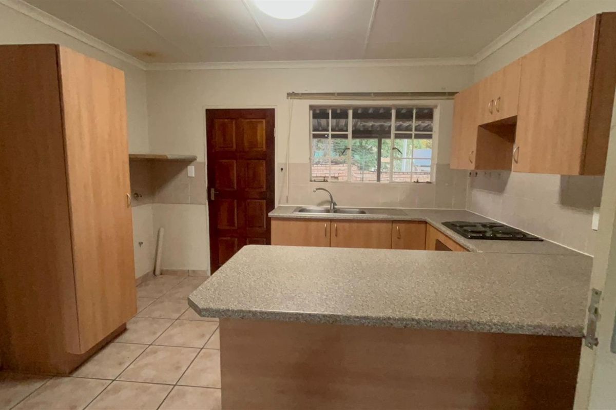 A functional kitchen featuring laminate cabinetry, stone-look countertops, a built-in gas hob, and tiled flooring, offering a blank canvas for potential updates.