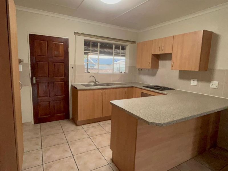 A functional kitchen featuring laminate cabinetry, stone-look countertops, a double bowl sink, and a built-in gas hob with tiled flooring and backsplash.