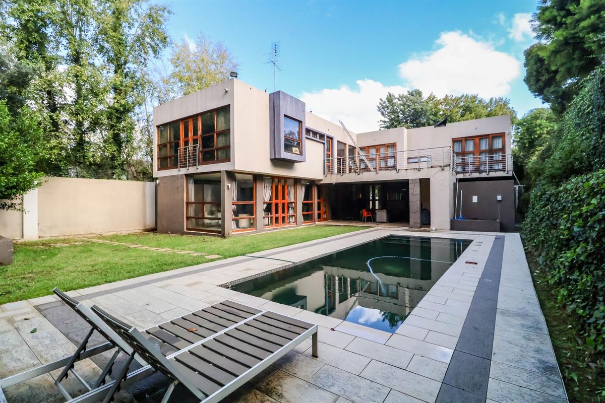 Rear view of a modern two-story house featuring a swimming pool, tiled patio area, and a balcony overlooking the garden.