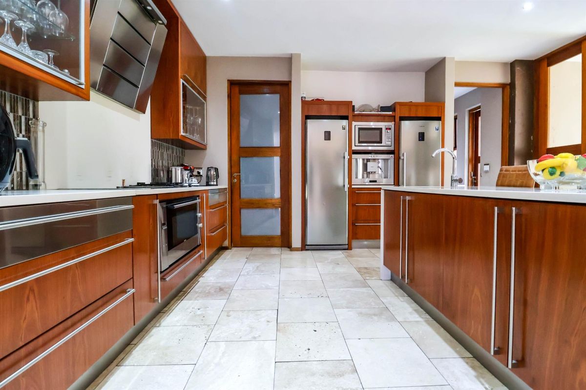 Modern kitchen featuring warm wood cabinetry, stone countertops, integrated appliances, and high-quality stone floor tiles.