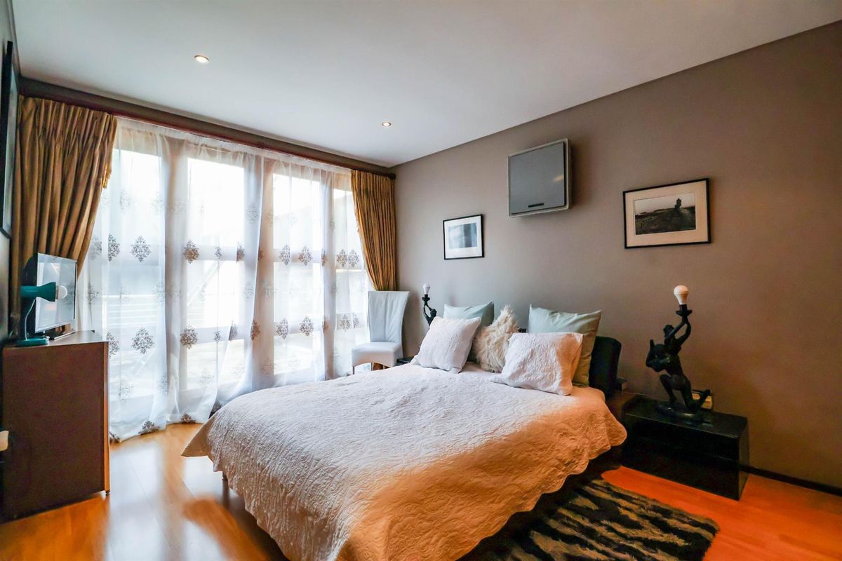 A well-lit bedroom featuring laminate flooring, recessed downlighting, and a wall-mounted air conditioning unit, offering a comfortable and functional living space.