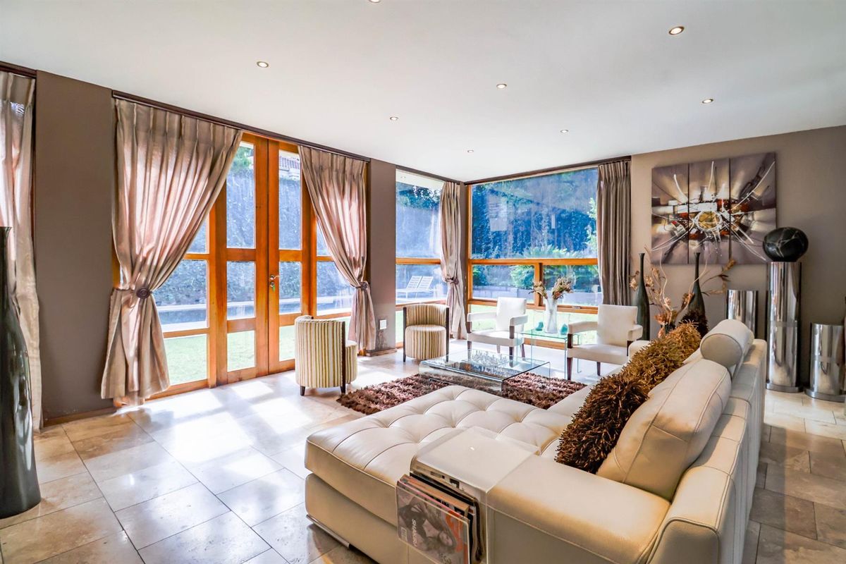 Spacious living room featuring large timber-framed glass doors and windows, stone flooring, and recessed downlighting, offering a bright and airy atmosphere.