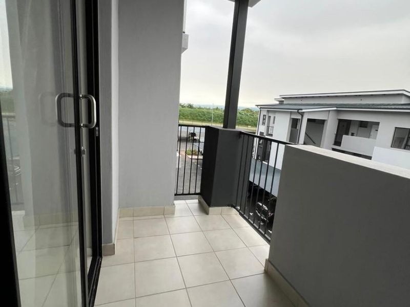 A clean, covered balcony featuring tiled flooring and a modern metal balustrade, offering an outdoor extension to the apartment living space.