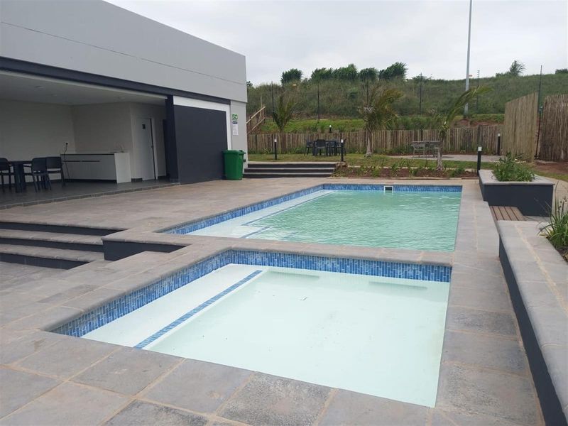 Communal pool area featuring a tiled swimming pool, paved surround, and a covered patio space with a built-in counter.