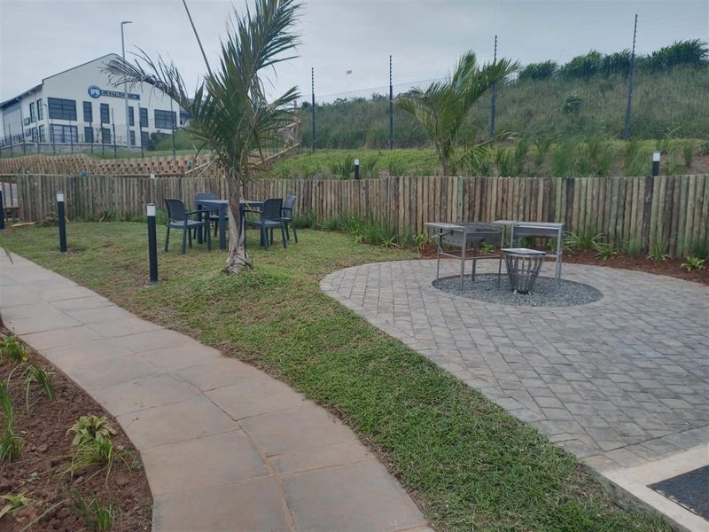 A landscaped garden area featuring a paved walkway, a circular paved patio section, timber fencing, and security perimeter fencing.