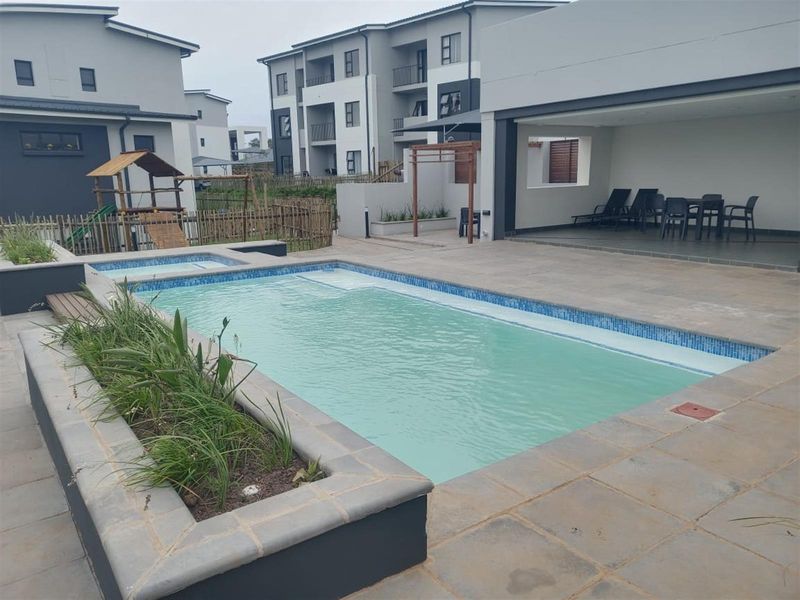 A well-maintained communal pool area featuring a tiled swimming pool, built-in planter, and a spacious covered patio for outdoor relaxation.