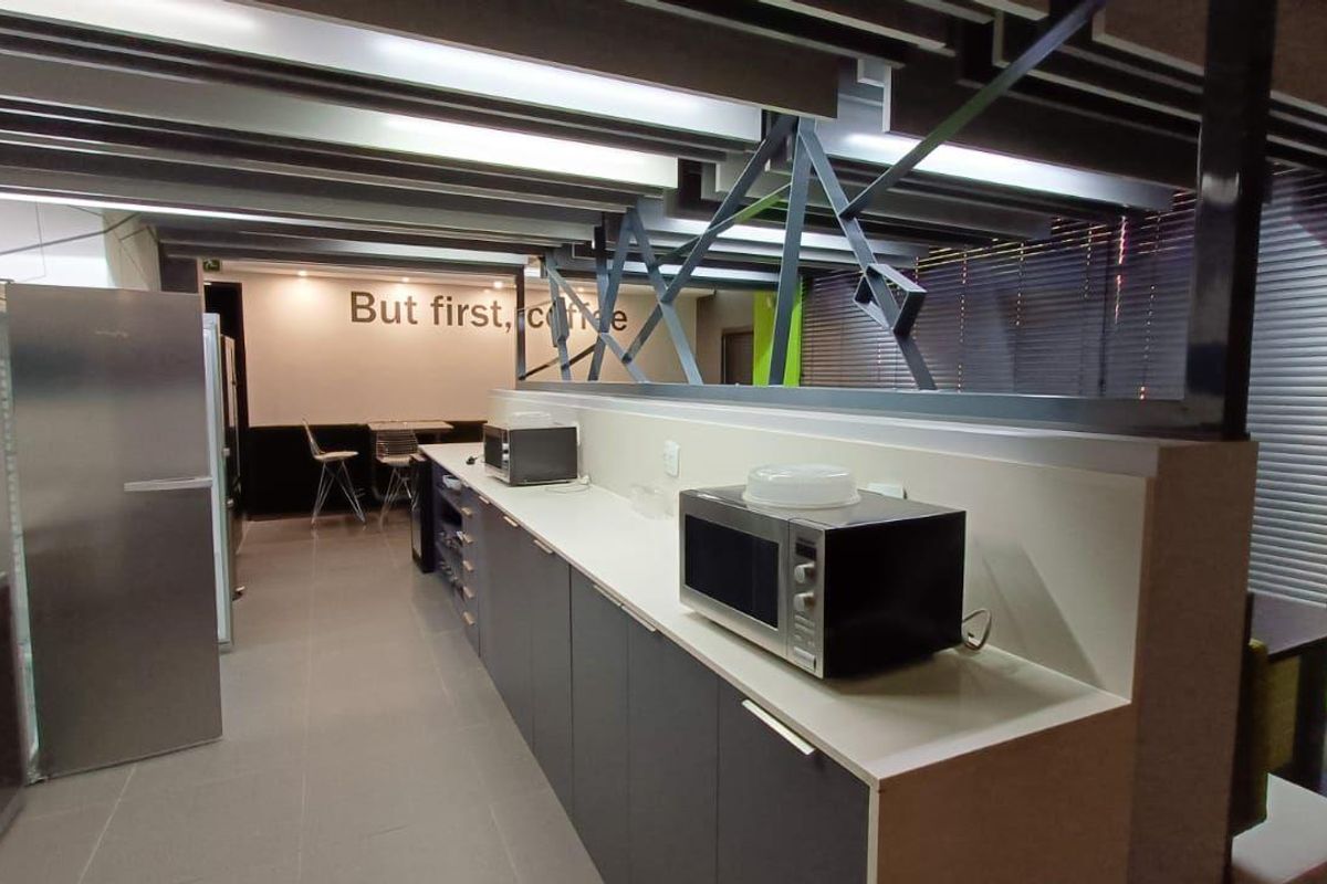 Modern commercial kitchenette featuring sleek grey cabinetry, integrated appliances, and an open-plan layout with industrial-style exposed ceiling beams.