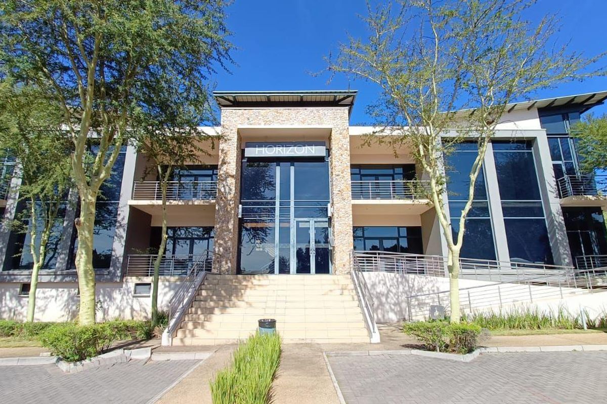 Modern commercial office building facade featuring large glass curtain walls, stone cladding accents, and a central elevated entrance with stairs.