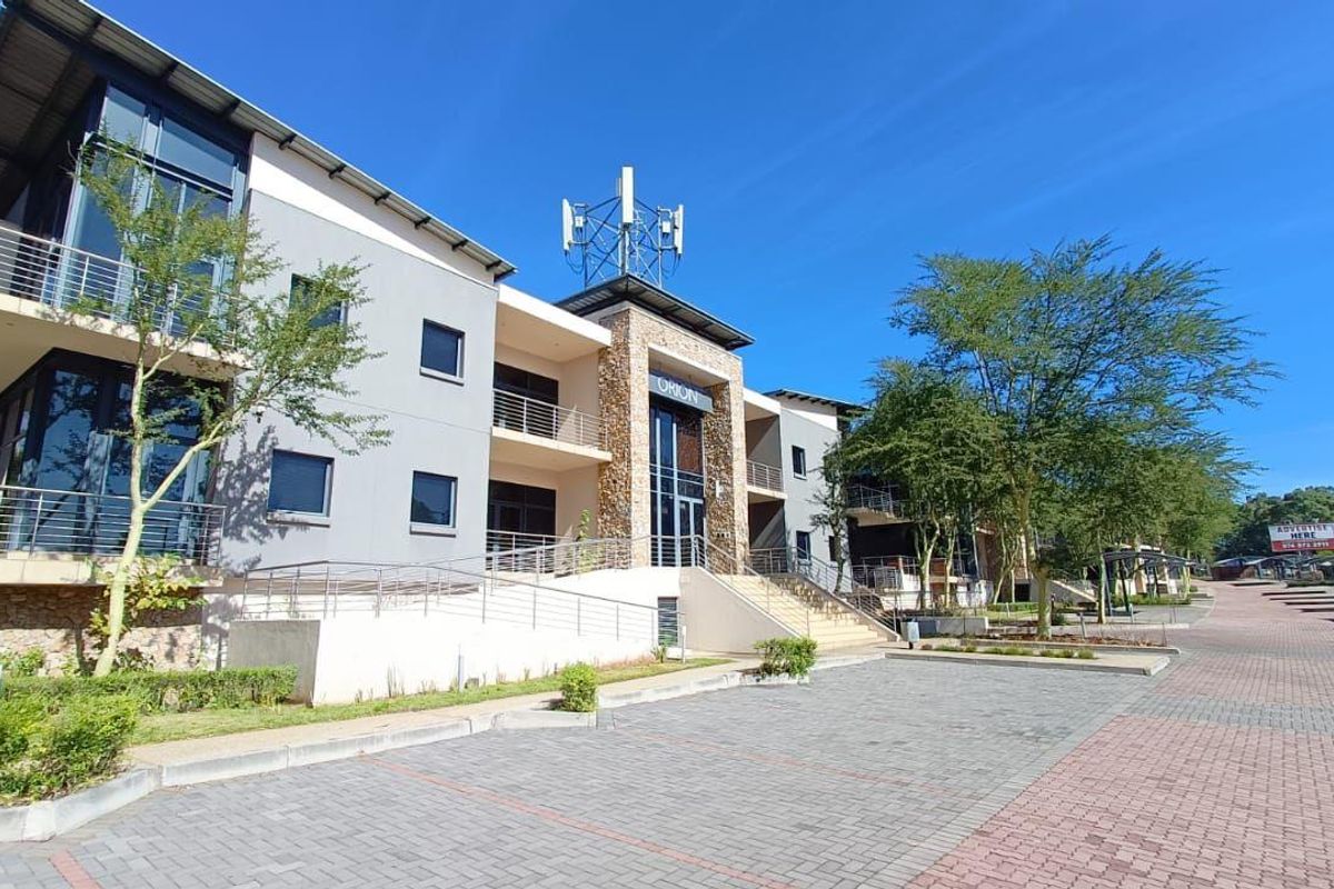 Modern commercial office building exterior featuring stone cladding, glass facades, balconies, and paved parking area.
