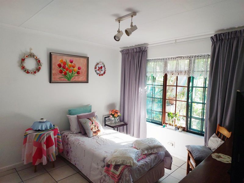 A cozy bedroom featuring tiled flooring, a multi-pane window with natural light, and adjustable track lighting.