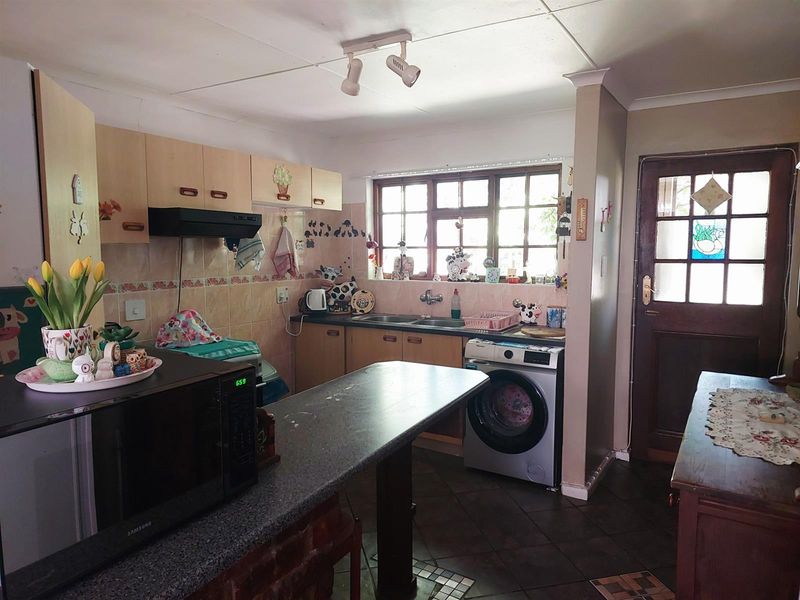 Functional kitchen featuring laminate cabinetry, double bowl sink, tiled splashback, breakfast bar, and direct access to the exterior via a timber door.
