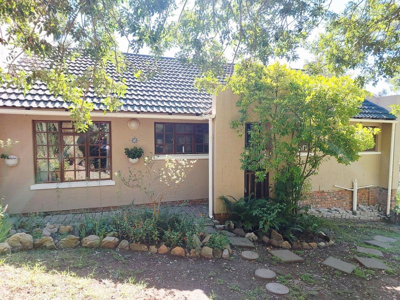 Front elevation of a single-story house featuring a tiled roof, timber-framed windows, and a textured plaster facade with a paved garden walkway.