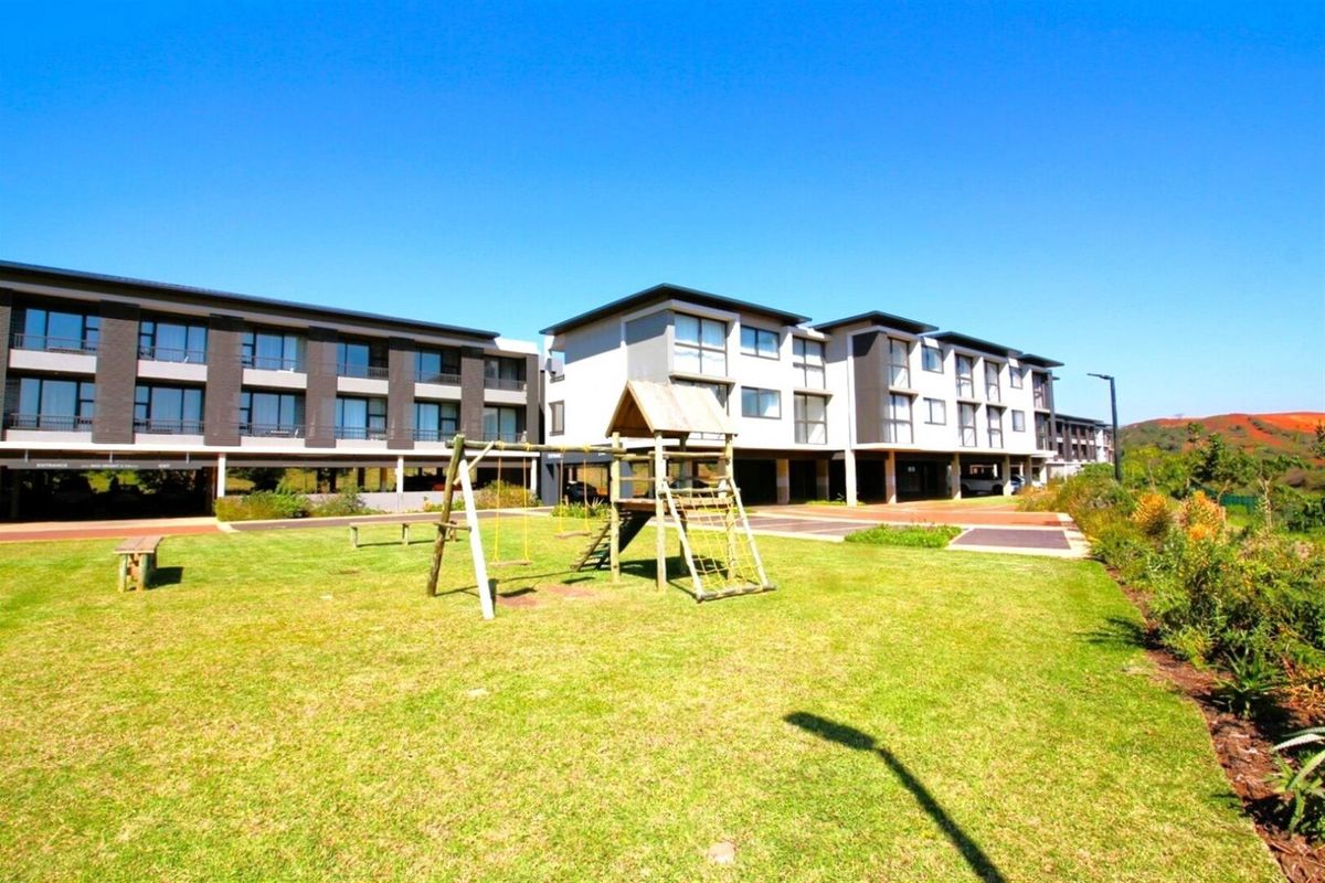 A view of the apartment complex exterior featuring a well-maintained lawn, paved driveway, and covered parking facilities.