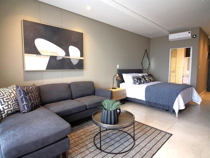 A modern open-plan studio apartment featuring tiled flooring, recessed lighting, and a split-system air conditioner, with an integrated bedroom and en-suite bathroom.