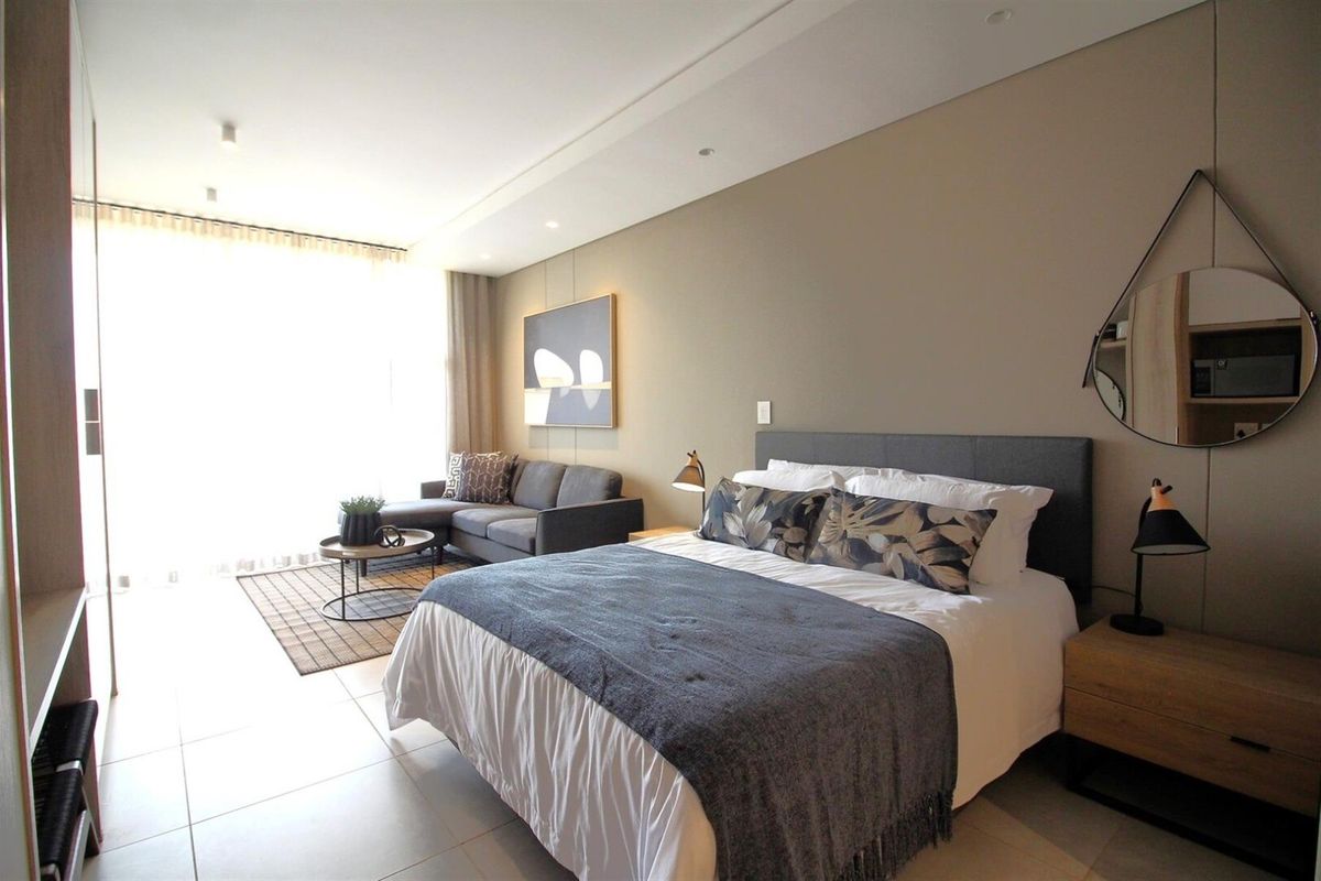 A modern, well-lit bedroom featuring neutral tones, tiled flooring, recessed ceiling lighting, and integrated storage solutions.