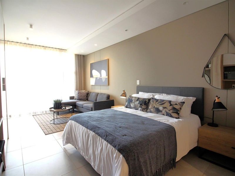 A modern, well-lit bedroom featuring neutral tones, tiled flooring, recessed ceiling lighting, and integrated storage solutions.