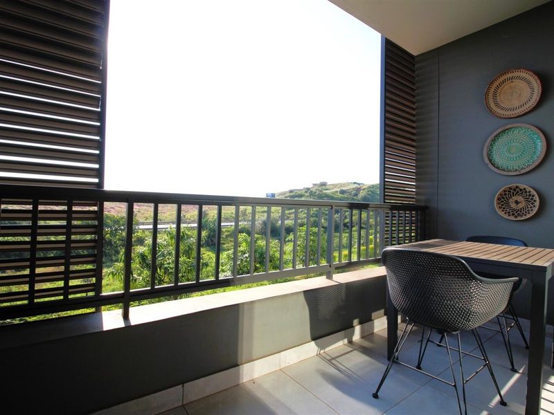 A modern covered balcony featuring tiled flooring, a metal balustrade, and adjustable privacy shutters, offering an open view of the surrounding landscape.