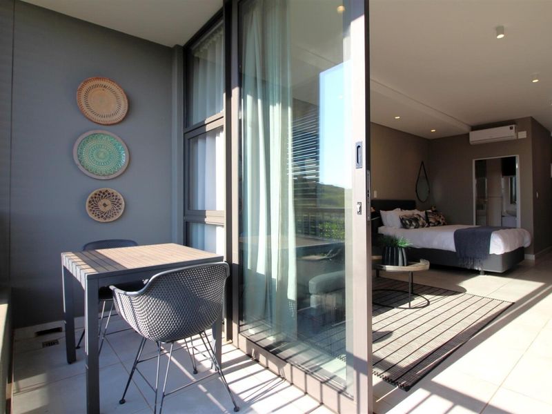 A modern covered balcony featuring tiled flooring and a large sliding glass door providing seamless access to the adjacent bedroom.