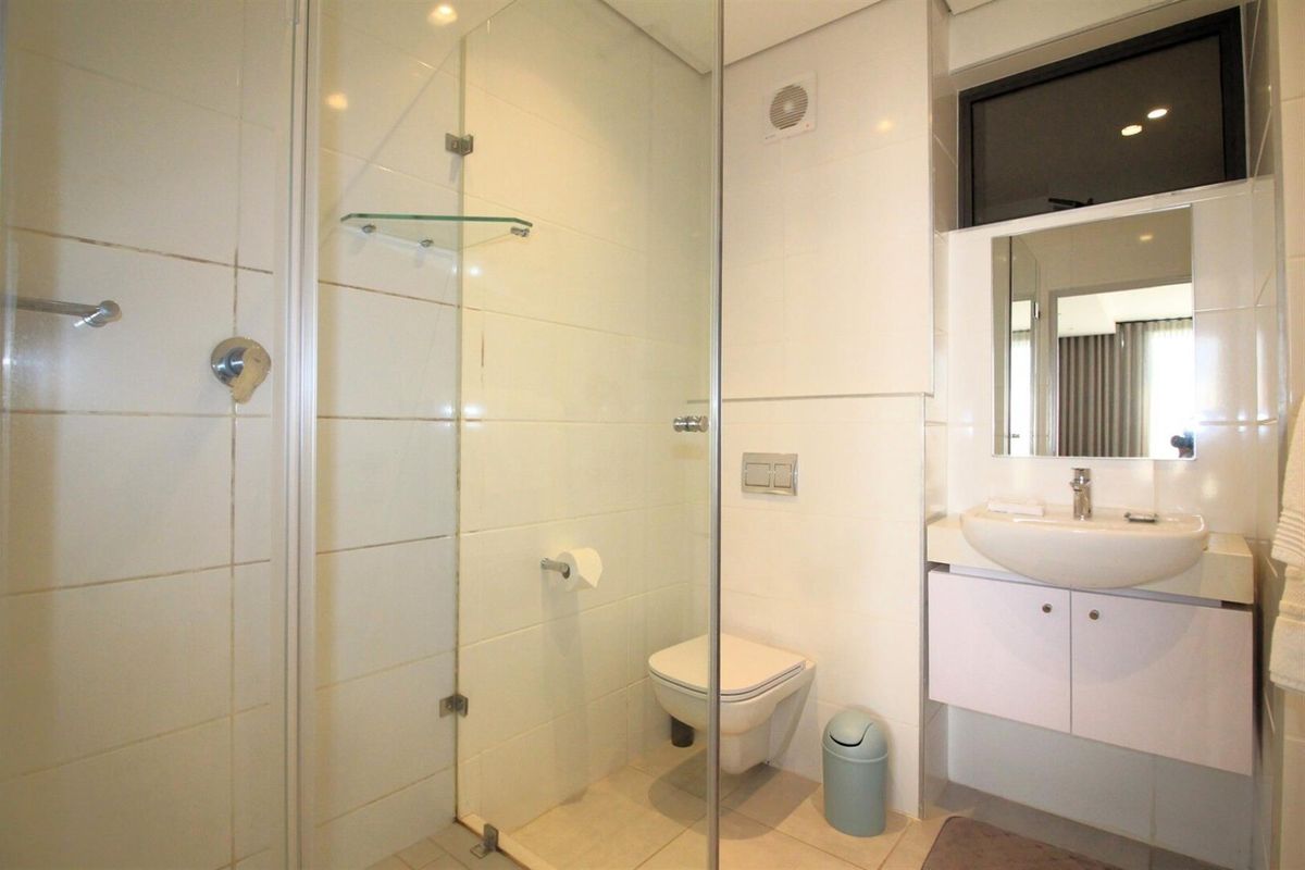 A clean, modern bathroom featuring a glass-enclosed shower, wall-mounted toilet, and a vanity unit with a basin.