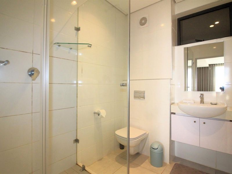 A clean, modern bathroom featuring a glass-enclosed shower, wall-mounted toilet, and a vanity unit with a basin.