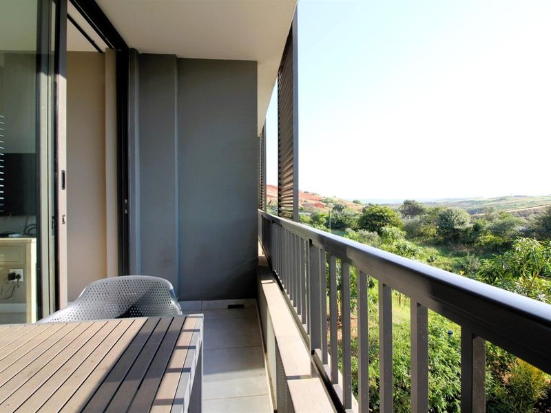 A modern balcony featuring tiled flooring, a metal balustrade, and a sliding glass door, offering scenic views of the surrounding landscape.
