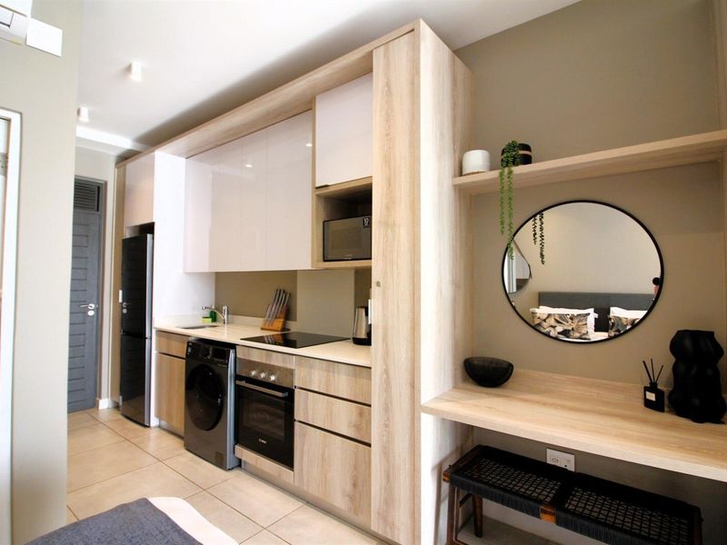 Modern open-plan kitchen featuring sleek wood-tone cabinetry, integrated appliances, and a built-in desk area with contemporary finishes and tiled flooring.