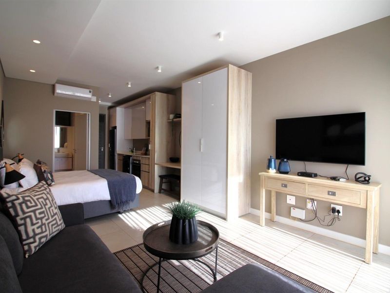Modern open-plan studio apartment featuring a kitchenette, built-in wardrobe, tiled flooring, and integrated air conditioning, offering a functional and contemporary living space.
