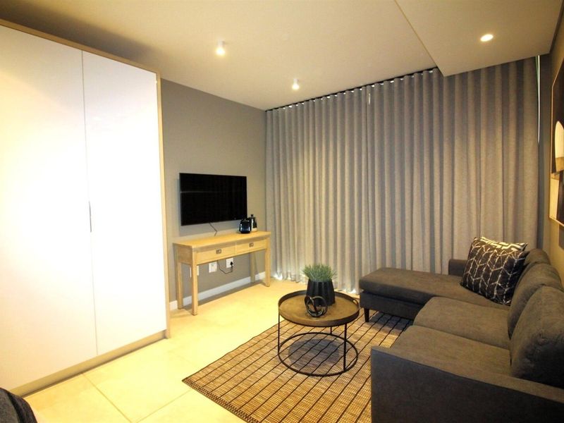 A modern living room featuring neutral tones, tiled flooring, recessed downlighting, and a large built-in wardrobe for storage.