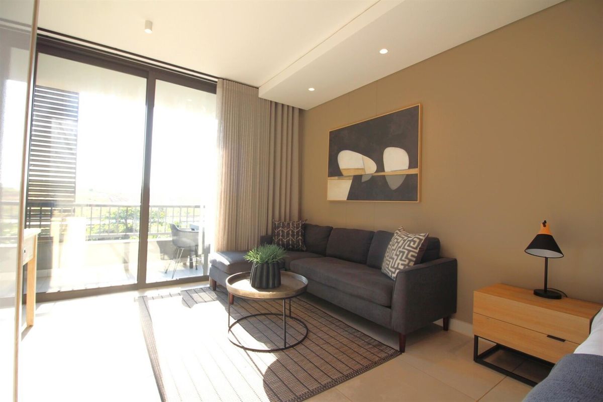 A modern, well-lit living room featuring large sliding glass doors that provide access to a private balcony and ample natural light.