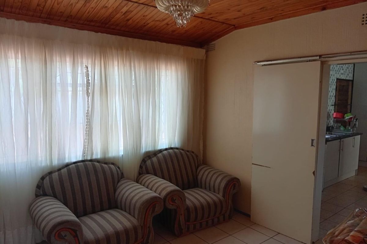 A living area featuring a timber-clad ceiling, tiled flooring, and a sliding door leading to an adjacent kitchen space.
