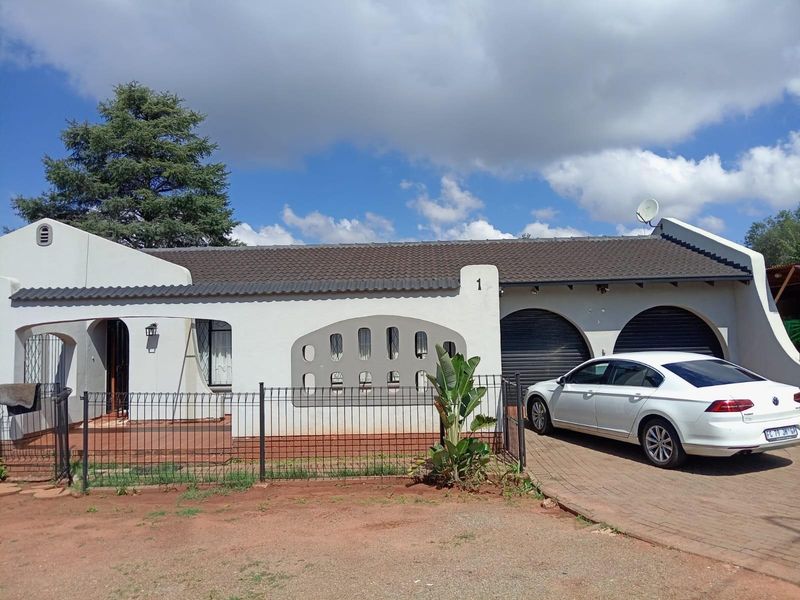 Front elevation of a single-story house featuring a tiled roof, arched garage doors, and a paved driveway with perimeter fencing.