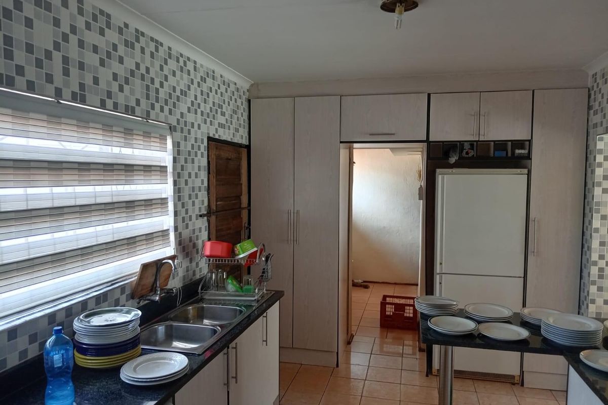 A functional kitchen featuring light-toned cabinetry, granite countertops, a double-basin sink, and tiled flooring with a mosaic-tiled backsplash.