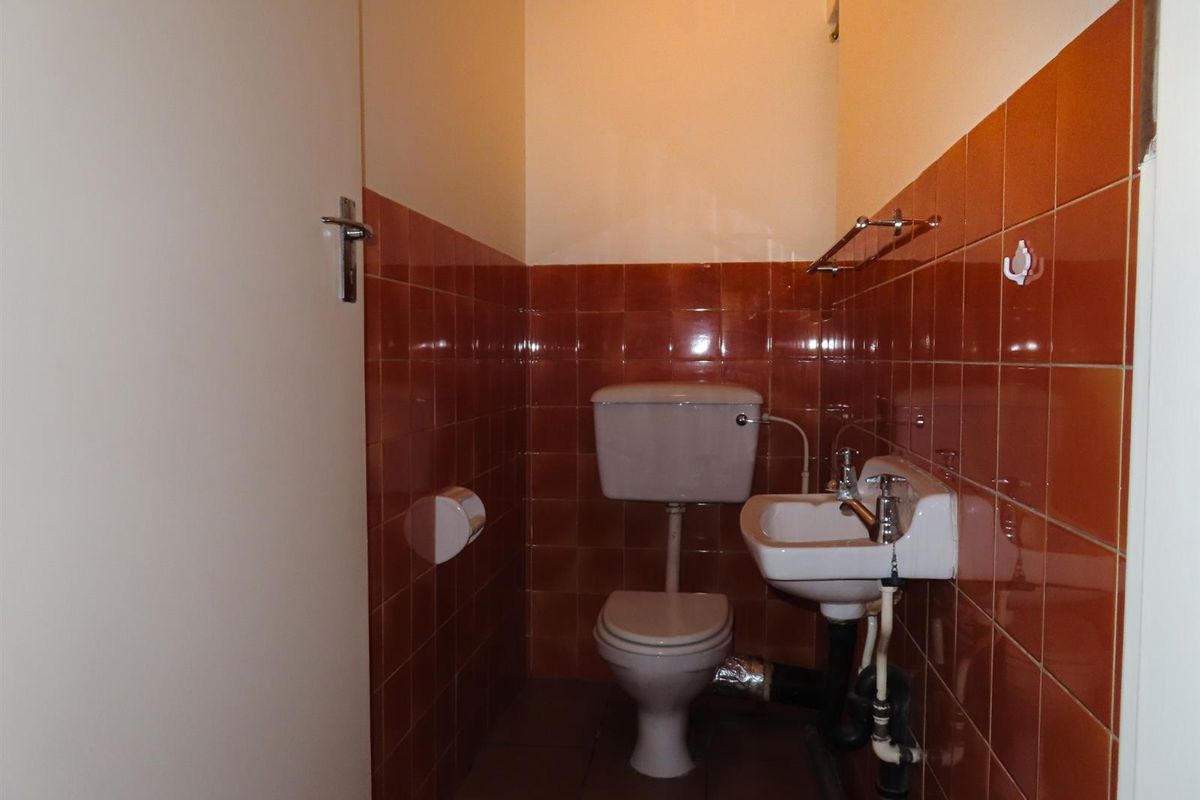A compact guest bathroom featuring a standard toilet, wall-mounted basin, and dated orange wall tiling.