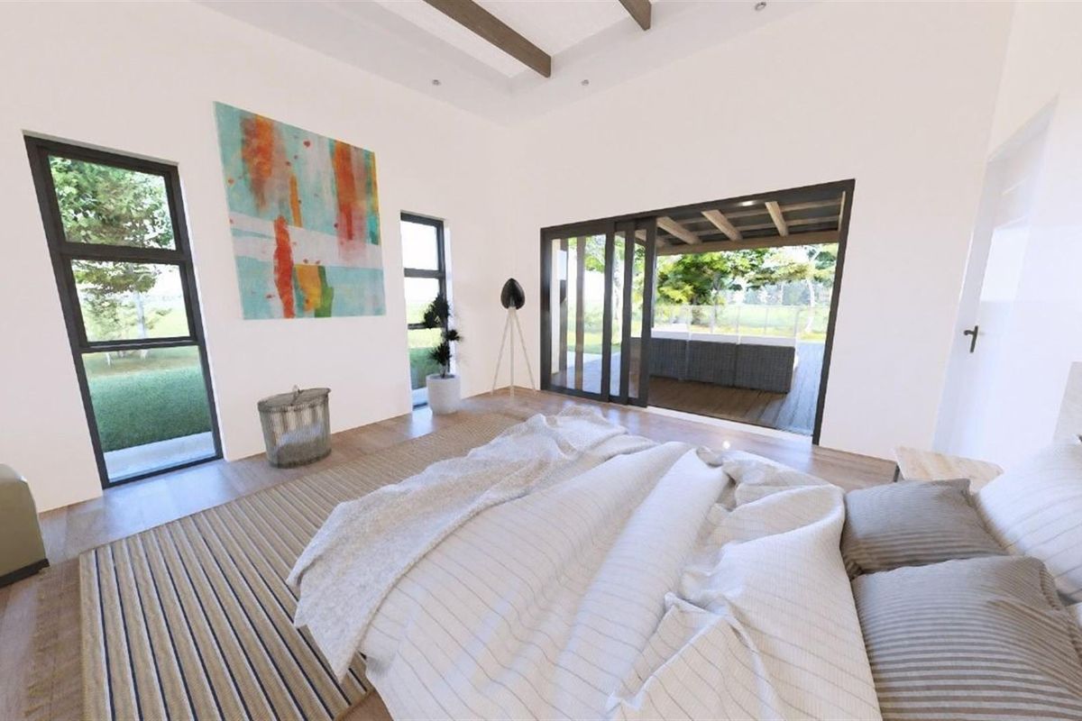 A bright, modern bedroom featuring exposed ceiling beams, large windows, and sliding glass doors that open onto a covered patio area.