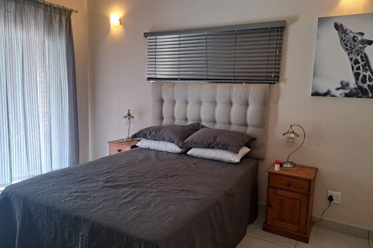 A well-maintained bedroom featuring tiled flooring, wall-mounted lighting, and a window fitted with horizontal blinds and sheer curtains.