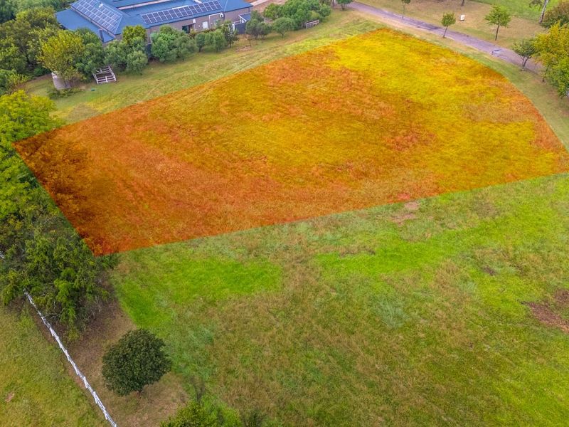 An aerial view of a vacant residential plot featuring established trees and grass, highlighting the property boundaries within a quiet neighborhood setting.