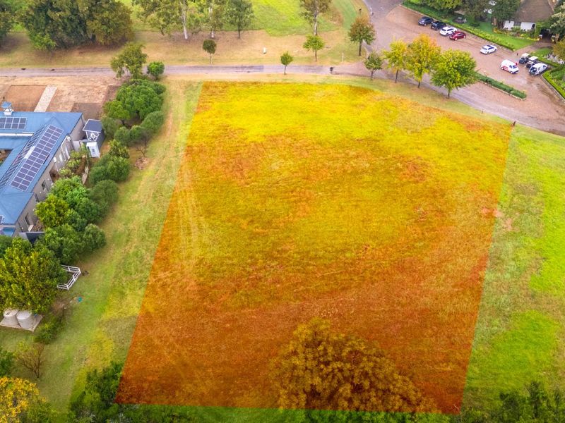 Aerial view of a vacant residential plot highlighted in orange, situated within a landscaped estate setting with established trees and nearby road access.