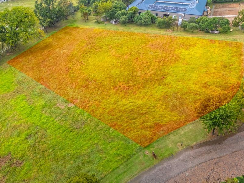 An aerial view of a vacant residential plot featuring open grass land with established trees and surrounding rural landscape.