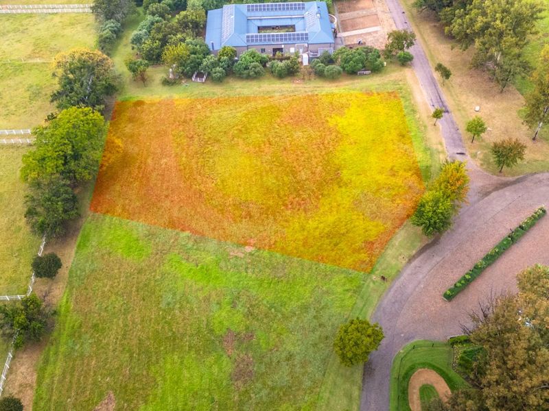 An aerial view of a vacant residential plot highlighted in a rural estate setting, featuring surrounding greenery and established access roads.