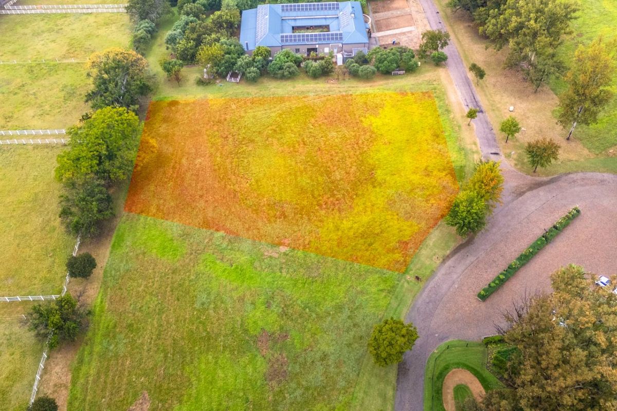 An aerial view of a vacant residential plot highlighted in a rural estate setting, featuring surrounding greenery and established access roads.