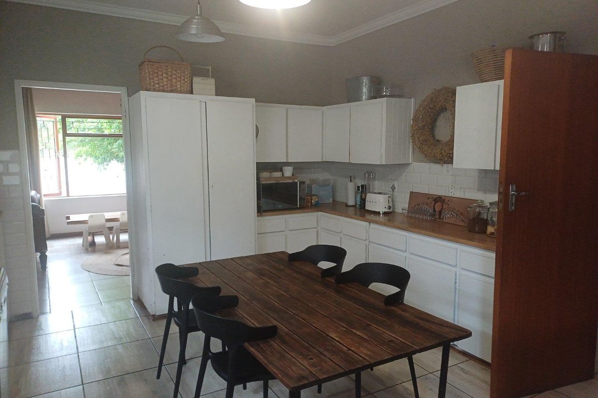 A functional kitchen featuring white cabinetry, wooden countertops, and tiled flooring, with an adjacent dining area and direct access to an exterior space.