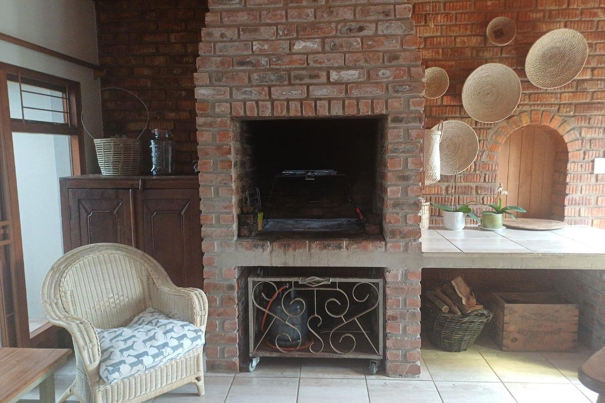 A rustic indoor braai area featuring a large exposed brick fireplace, tiled flooring, and built-in preparation counter space.