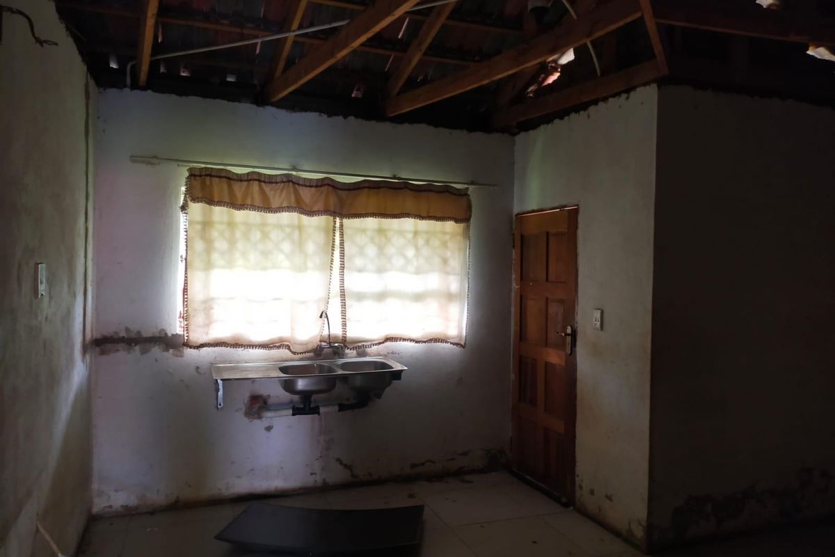 A dilapidated interior space featuring an exposed roof structure, basic double sink, and damaged wall finishes, requiring significant renovation and structural repairs.