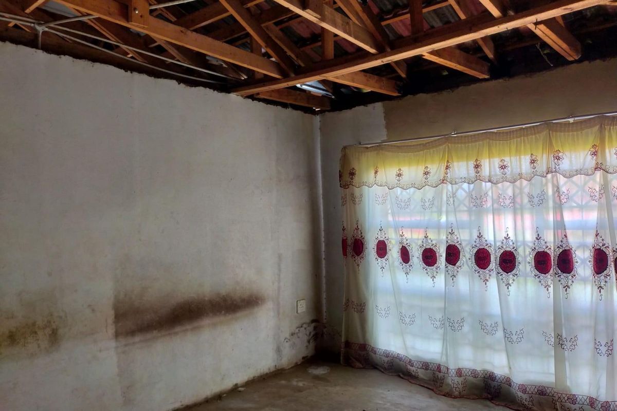 An unfinished bedroom interior featuring exposed timber roof trusses, missing ceiling, and visible wall staining, requiring significant renovation and finishing work.