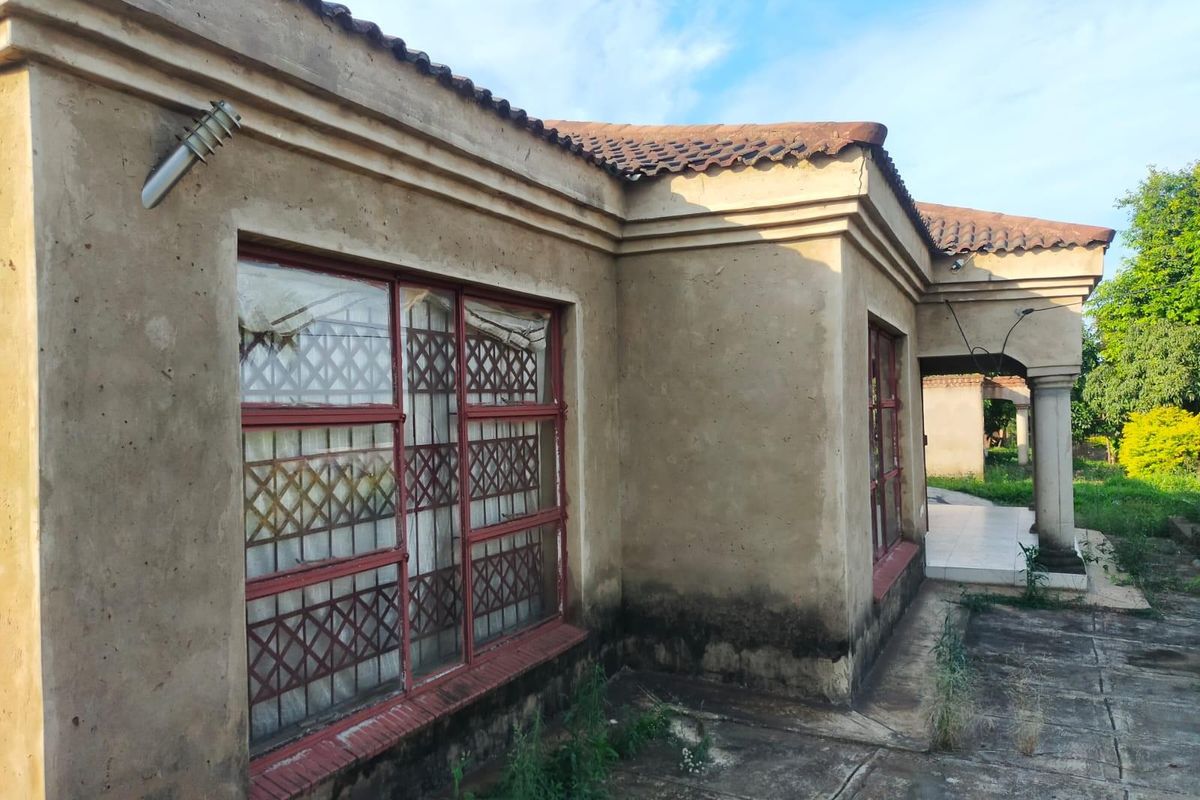 Exterior view of a house showing significant wear to the plaster facade, weathered window frames, and overgrown paved areas requiring maintenance and restoration.