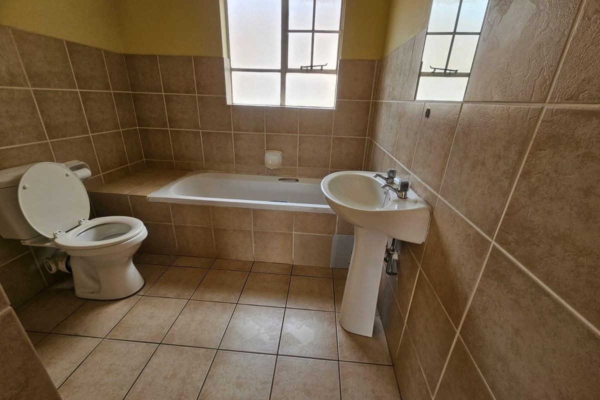 A functional bathroom featuring a pedestal basin, built-in bathtub, and toilet, finished with neutral ceramic wall and floor tiling.