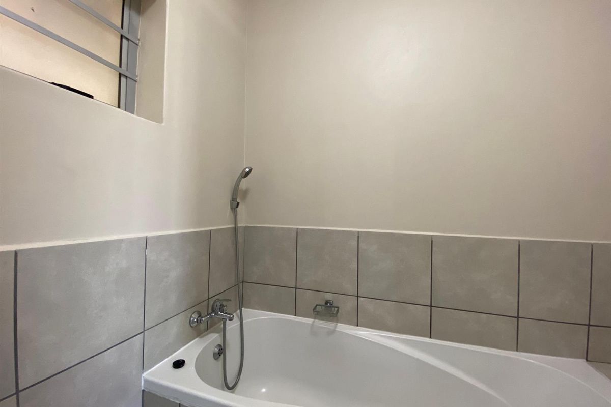 A clean, functional bathroom featuring a built-in bathtub with a handheld shower mixer and neutral wall tiling.
