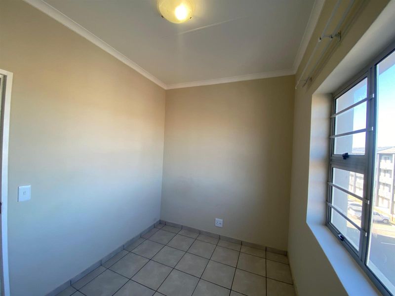 An empty bedroom featuring tiled flooring, neutral walls, and a window fitted with security bars.
