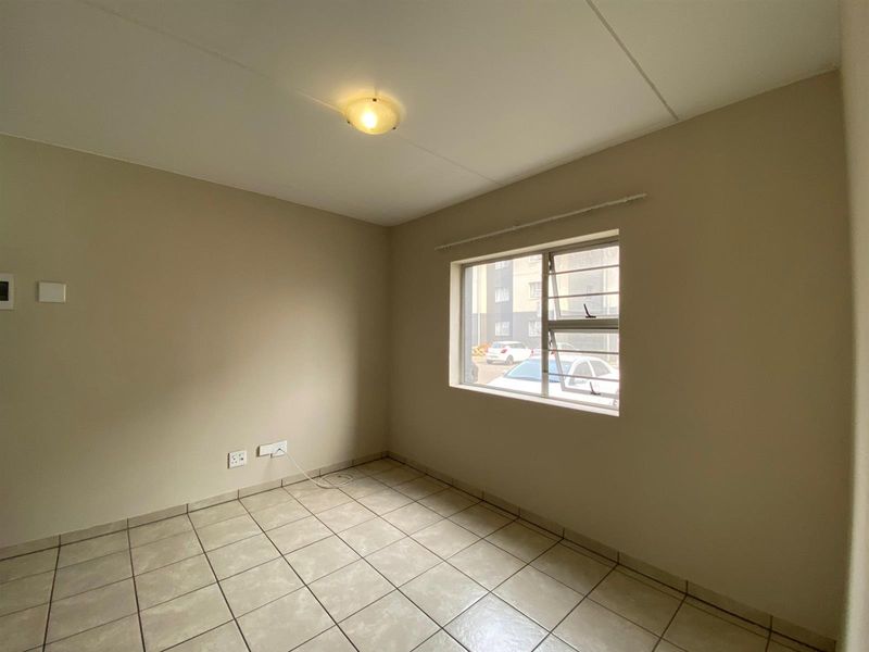 A clean, empty bedroom featuring neutral wall paint, tiled flooring, and a window providing natural light.