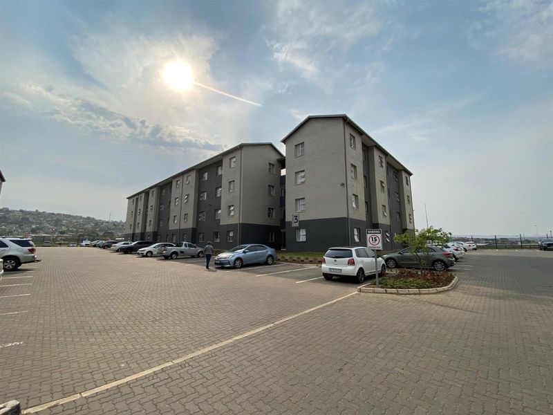 Exterior view of a multi-story apartment complex featuring a paved parking area and landscaped garden beds.